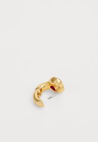 Pendiente de aro en tono dorado con diseño curvado. Acabado metálico suave, con parte superior redondeada y un pequeño acento interior rojo.