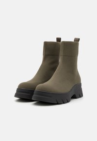 Botoșei verzi măslinii până la gleznă, cu țesătură nervurată, talpă din cauciuc negru masiv și curele pentru a fi ușor de încălțat.