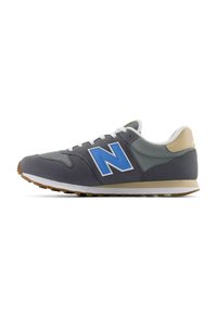 Sneaker atletiche grigie con upper in rete, logo "N" blu, lacci bianchi e accenti beige chiaro sul tallone, dotate di suola in gomma.