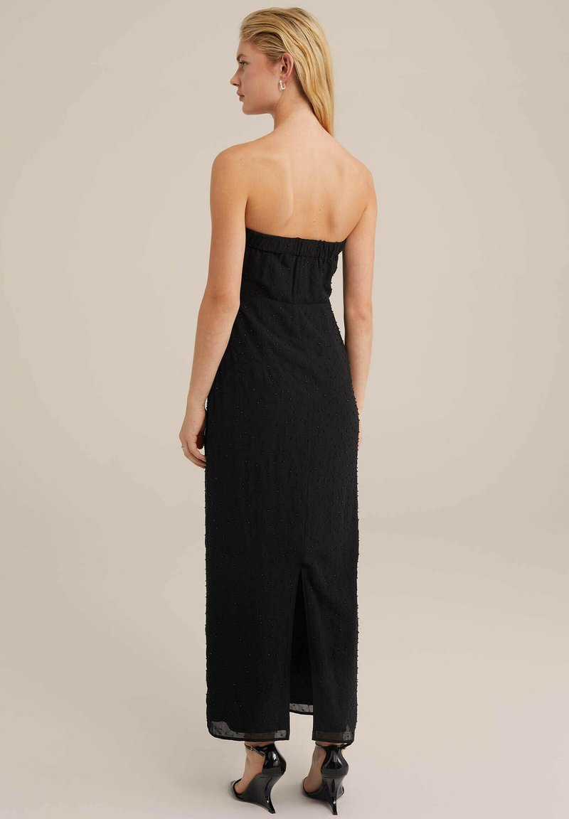 Vestido negro sin tirantes con tejido texturizado, con una silueta larga, abertura en la parte trasera y un corsé ajustado con detalles fruncidos.