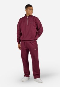 Burgundin väri sweatshirt ja housut pehmeästä materiaalista. Varustettu vetoketjukauluksella ja logot yksityiskohdalla. Yhdistetään valkoisiin lenkkareihin kontrastia varten.