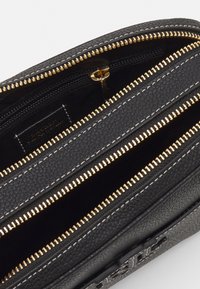 Svart texturerad läderväska med tre fack, gulddragkedjor och en slät foder. Funktioner inkluderar sömnadsdetaljer och en dragkedjeficka.