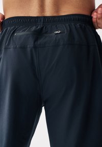 Shorts de sport navy avec une taille élastique, dotés d'une poche zippée à l'arrière et d'un tissu lisse et léger pour un confort optimal.