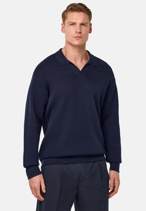 Navy pullover met een v-hals en lange mouwen, gemaakt van textuurstof. Gekenmerkt door een casual pasvorm, gecombineerd met donkere broeken.