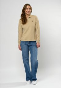 Beige langemouwen poloshirt met een kraag, voorzien van een klein logo. Gepaard met lichtblauwe flared jeans en witte sneakers. Eenvoudig ontwerp.