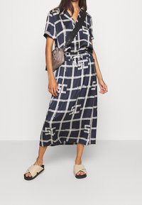 Ensemble coordonné à motif marine en design de grille, comprenant une chemise à manches courtes et une jupe longue, accompagnés de sandales à glisser beiges.