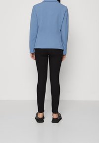 Svetle modrý saka na míru s klopovým límcem, zkombinované s černými slim-fit džíny a černými botami na slip-on, pohled zezadu.