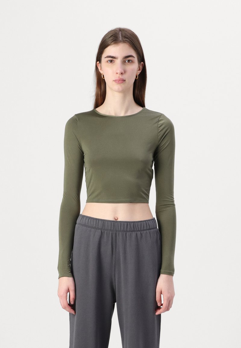 Olive green long-sleeve cropped top made of smooth fabric, paired with loose-fitting gray pants featuring an elastic waistband.