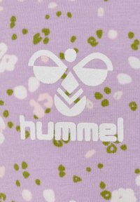 Jasnofioletowa tkanina ma fakturowaną powierzchnię z kwiatowym wzorem w kolorze zielonym i białym. Logo "hummel" jest wyraźnie wyeksponowane na białym tle.