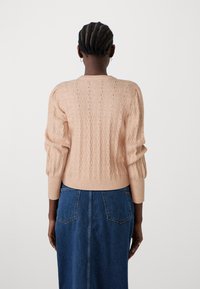 Pull en tricot rose clair avec un motif ondulé texturé, des poignets côtelés et un col rond. Porté sur une jupe en denim bleue.