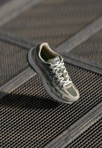 Beżowe i zielone siatkowe sneakersy z białymi sznurowadłami, z teksturowaną podeszwą i smukłym designem. Logo marki umieszczone na języku.
