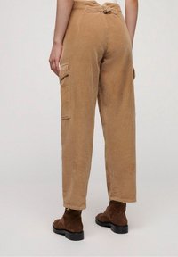 Lichtbruine corduroypantalon met een wijde pijp, voorzien van een riem in de taille en zij cargozakken. Getextureerde ribbelstof.