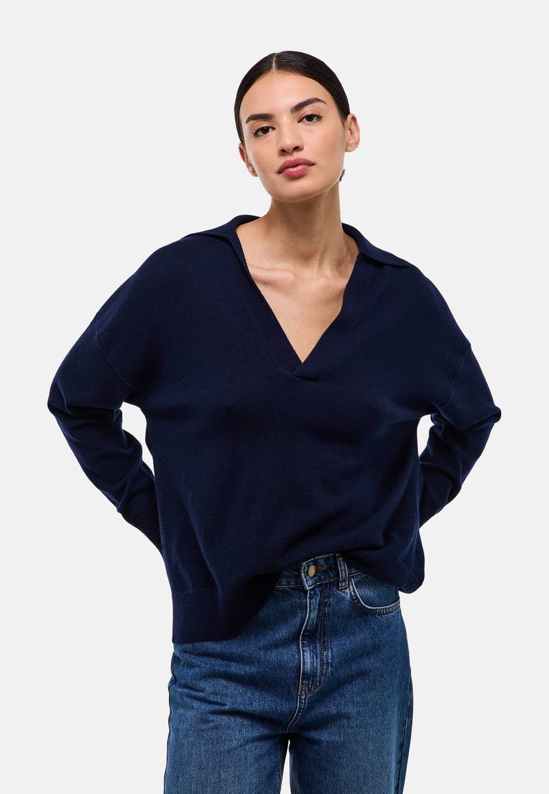 Pull en maille bleu marine avec un col en V, doté de manches longues et d'une coupe ample, associé à un jean bleu taille haute.