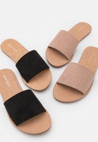 Deux paires de sandales à enfiler : l'une en daim noir et l'autre en tissu beige. Les deux ont des larges brides et une semelle extérieure plate couleur tan.