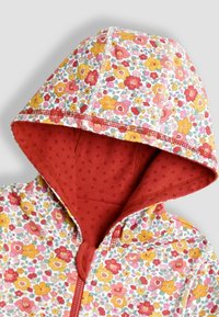 Felpa con zip a motivo floreale caratterizzata da uno sfondo bianco con fiori rossi, arancioni e gialli. L'interno del cappuccio è di un rosso uniforme con un motivo a pois. Materiale in cotone.