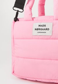 Roosa pehmenduskotid pehmest kangast, millel on kaks sangaga ja reguleeritav rihm. Sildil on musta värvi tekst "MADS NØRGAARD COPENHAGEN."