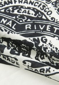 Bomullsstoff med et svart og hvitt trykt mønster som inneholder tekst og dekorative elementer, og skaper et teksturert, lagdelt utseende.