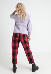 Lila stickad tröja med ribbat mönster, ihop med röda rutig höga byxor med svarta detaljer och smalnade ben. Svarta ankelstövlar.