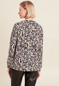 Langarmshirt met een zwart, wit en oranje bloemenpatroon. Heeft een ontspannen pasvorm en een zachte, gestructureerde stof. Eenvoudige ronde halslijn.