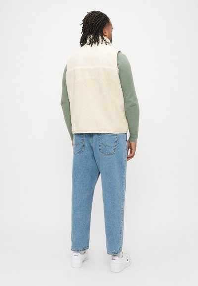 Colete de lã polar creme com textura suave, combinado com jeans de cintura alta azul claro e ténis brancos, visto de costas.