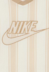 Αθλητική φανέλα της Nike σε ανοιχτό εκρού χρώμα με κάθετες ρίγες. Διαθέτει ευδιάκριτο λευκό κεντημένο λογότυπο και γιακά σε σχήμα V σε μπεζ απόχρωση.