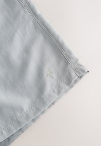 Lichtgrijze korte broek gemaakt van zachte stof, met een palmboomborduursel in lichte draad op de onderste linkerzoom, voorzien van nette stikdetails.