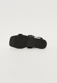 Svarte sandaler med flat såle, med et glatt overmateriale, to justerbare stropper og en teksturert fotbunn for grep.