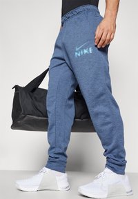 Blauwe fleece joggers met een elastische tailleband, voorzien van een lichtblauw Nike-logo op de bovenbeen. Gekocht met witte sneakers en een zwarte sporttas.