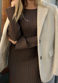Robe en maille côtelée marron associée à une veste texturée en mélange de laine de couleur crème. Comprend des manches longues avec poignets évasés et boutons.
