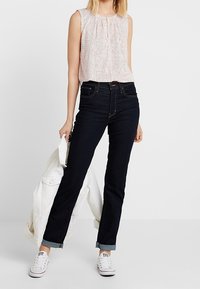 Biała bluzka bez rękawów z zakładkami, połączona z ciemnoniebieskimi dżinsami i białymi trampkami. Dżinsy podwinięte na mankietach, w ręku casualowa kurtka.