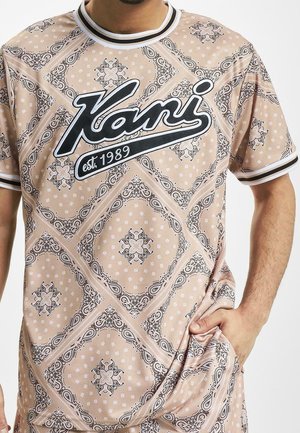 Kurzärmeliges T-Shirt in blassem Pfirsich mit schwarz-weiß gemustertem Design, großem "Kani"-Logo und geripptem Halsausschnitt mit Streifen.