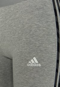 Leggings atléticos grises con una textura suave, que presentan un diseño de rayas negras y grises en el costado y un logo blanco de Adidas cerca de la cinturilla.