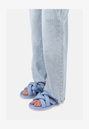 Light blue braided sandals with a thick, cushioned sole and textured strap, worn with light blue denim jeans.
