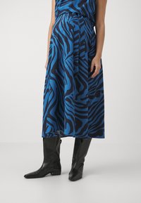 Sininen ja musta zebra-kuvioinen mekko, jossa on valuva muotoilu, polvipituinen helma ja sidottu vyötärö, yhdistettynä mustiin polvipitkiin saappaisiin.