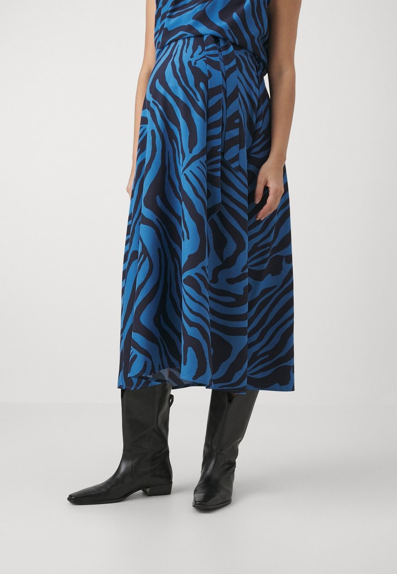 Sininen ja musta zebra-kuvioinen mekko, jossa on valuva muotoilu, polvipituinen helma ja sidottu vyötärö, yhdistettynä mustiin polvipitkiin saappaisiin.
