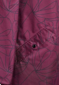 Tela burdeos con un patrón floral lineal en negro. Incluye un bolsillo lateral con cierre a presión negro. Textura suave.