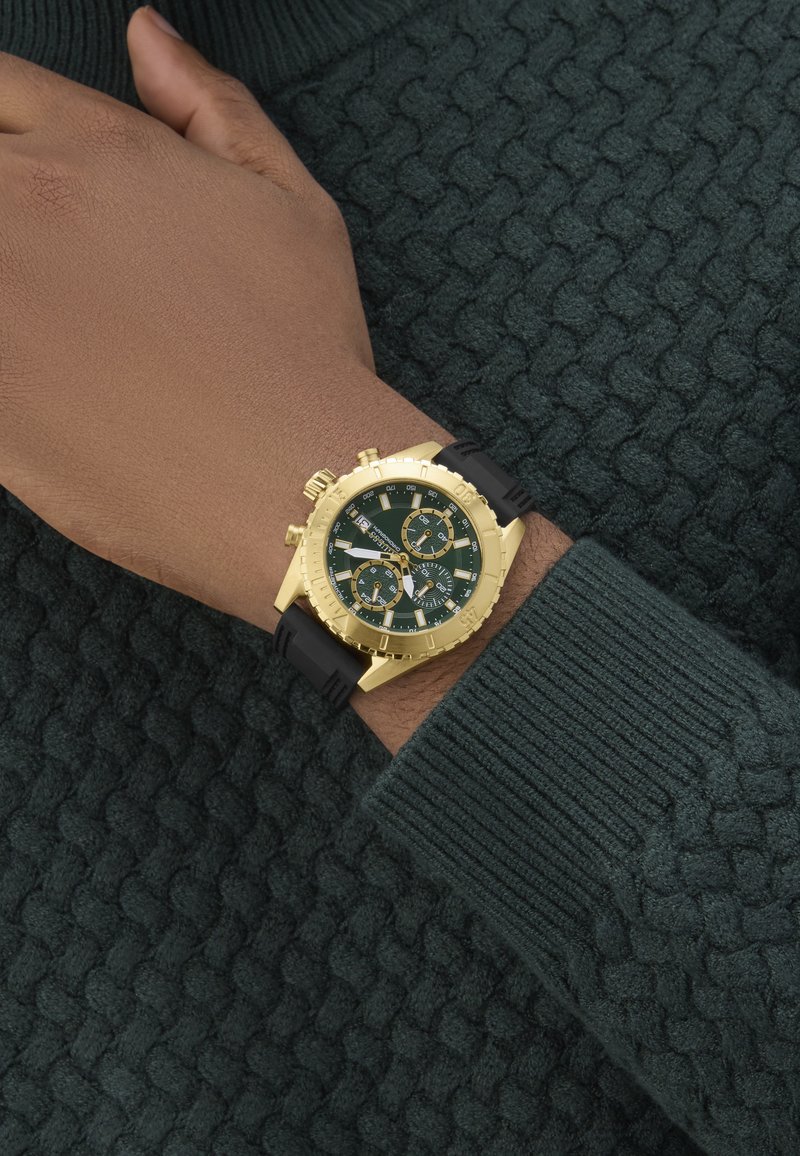 Orologio cronografo dorato con quadrante verde e cinturino in gomma nera, dotato di più sottoquadranti e dettagli dorati testurizzati.