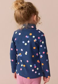 Marineblå langærmet top med farverige prikker i pink, orange, blå og grøn. Blødt bomuldsstof med en afslappet pasform og høj krave.