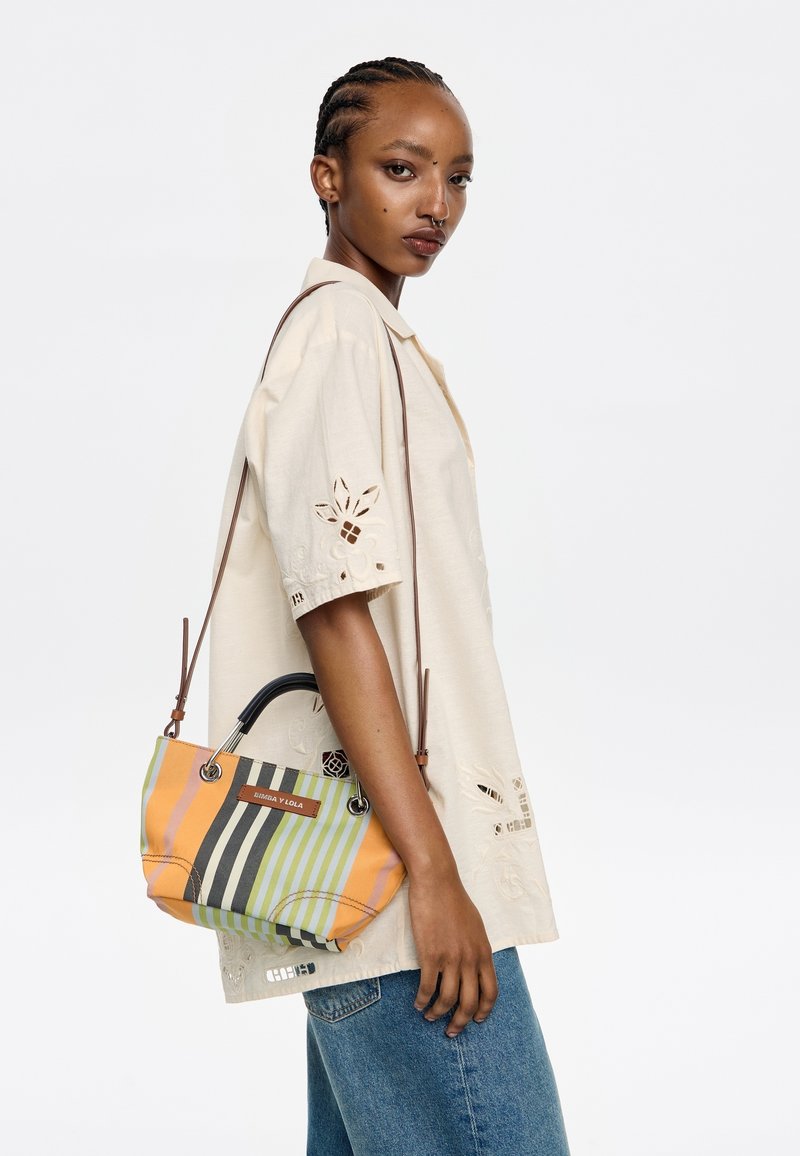 Colorful striped handbag with black and orange hues, featuring a curved handle, metal hardware, and a brand tag. Woven fabric texture visible.