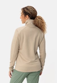 Pullover beige a maniche lunghe con collo alto, caratterizzato da un motivo a nido d'ape testurizzato e aperture per i pollici. Completato da pantaloni verdi.