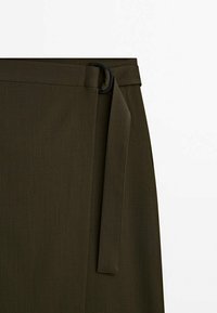 Jupe portefeuille vert olive foncé avec une ceinture en tissu passant par une boucle noire en forme de D.