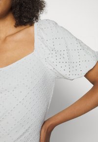 Top branco de mangas bufantes com tecido texturizado e padrões recortados. Decote quadrado e silhueta ajustada.