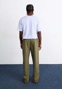 T-shirt curto de cor roxa clara com mangas curtas, combinado com calças largas, em verde oliva, vistas de trás. Tecido suave com cintura elástica.