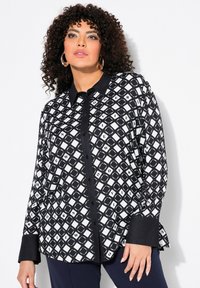 Blusa a maniche lunghe bianco e nero con un motivo geometrico a rombi, dotata di colletto, chiusura con bottoni e polsini a contrasto.