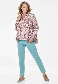Long-sleeve blouse in a pink and cream abstract pattern, paired with light teal pants. Model wears light brown sneakers.