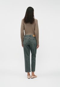 Pelēki džinsi ar brīvu piegriezumu, augstu vidukli un aizmugurējām kabatām. Apvienoti ar brūnu adītu džemperi. Audums ir mīksts, ar gludām šuvēm.