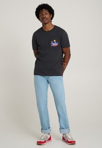 Dark gray cotton short-sleeve t-shirt featuring a colorful graphic design on the chest. Paired with light blue jeans and red-accented sneakers.