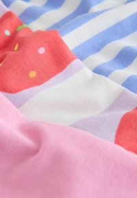 Primer plano de tela suave con rayas en tonos pastel rosa, blanco y azul, y áreas rojas decoradas con lunares coloridos.