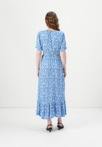 Robe maxi florale bleue avec manches courtes, taille élastique et ourlet volanté. Présente de petites fleurs blanches sur un fond bleu uni.