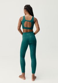Teal träningskläder set med en sport-bh som har en skärning i ryggen och mönstrade leggings i en texturerad design. Andningsbart, figurnära material.
